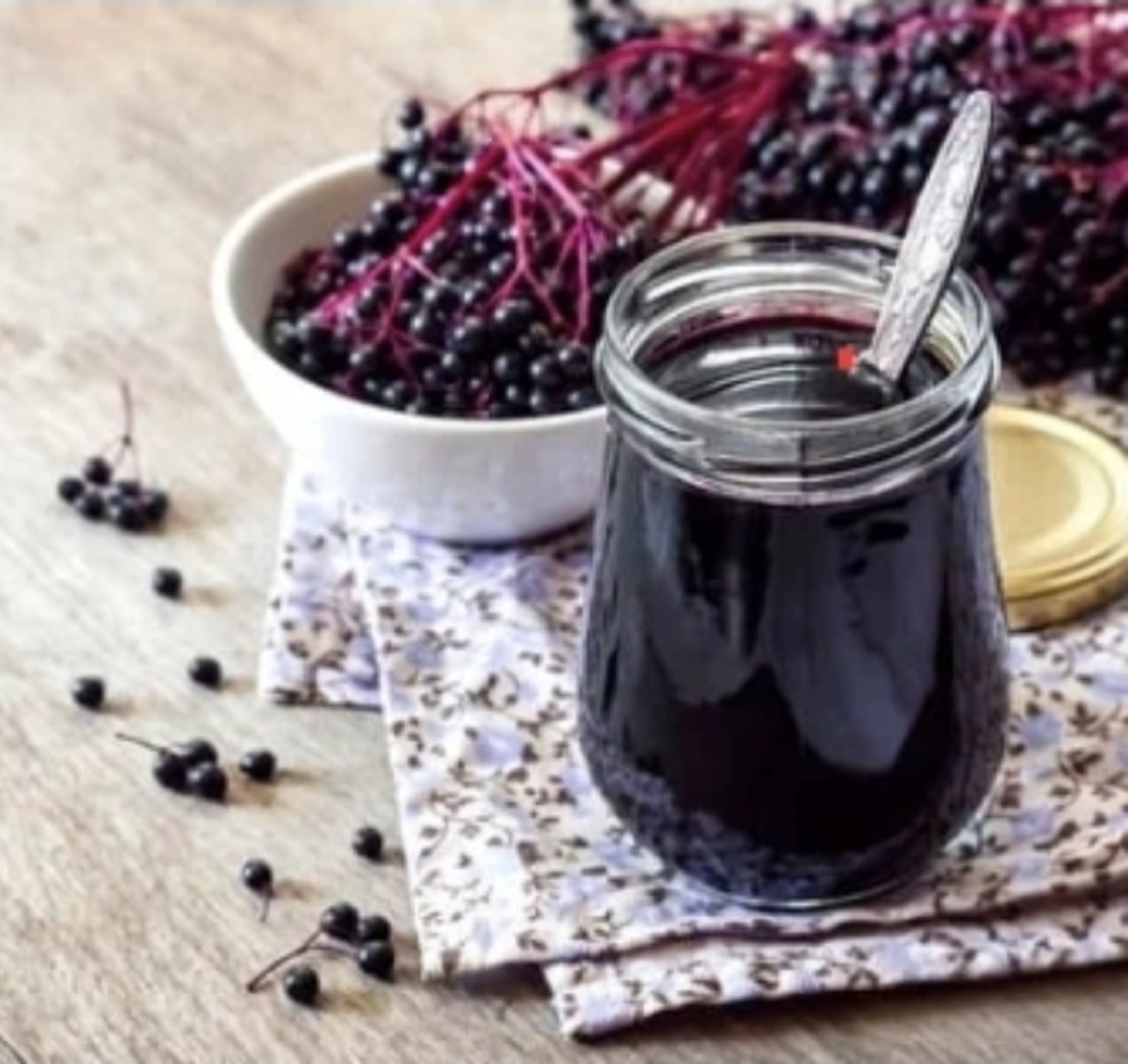 Glass mason jar of dark elderberry syrup with fresh elderberries
